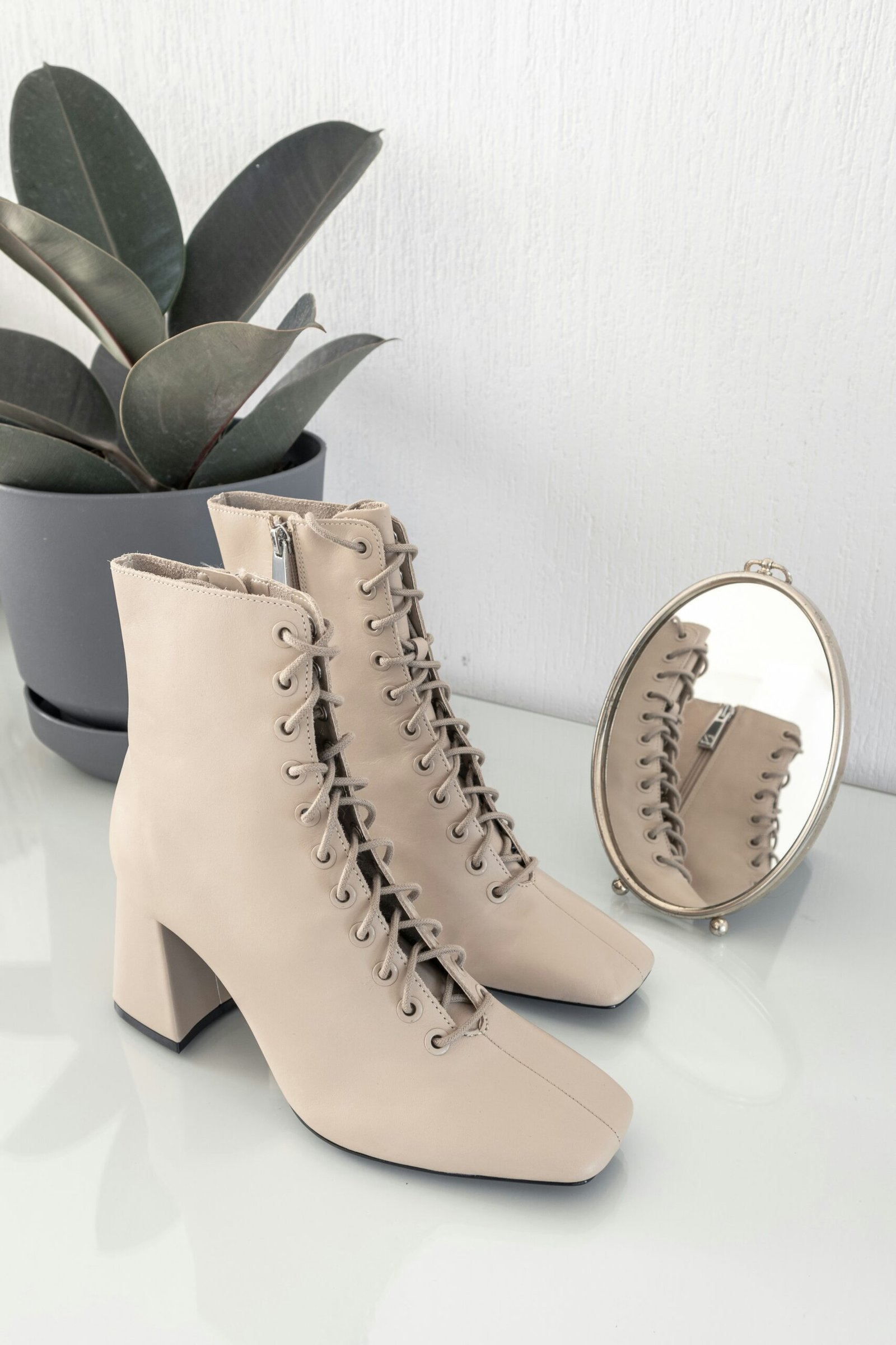 Women's cream lace-up ankle boots with block heels and side zipper on a white display table.
